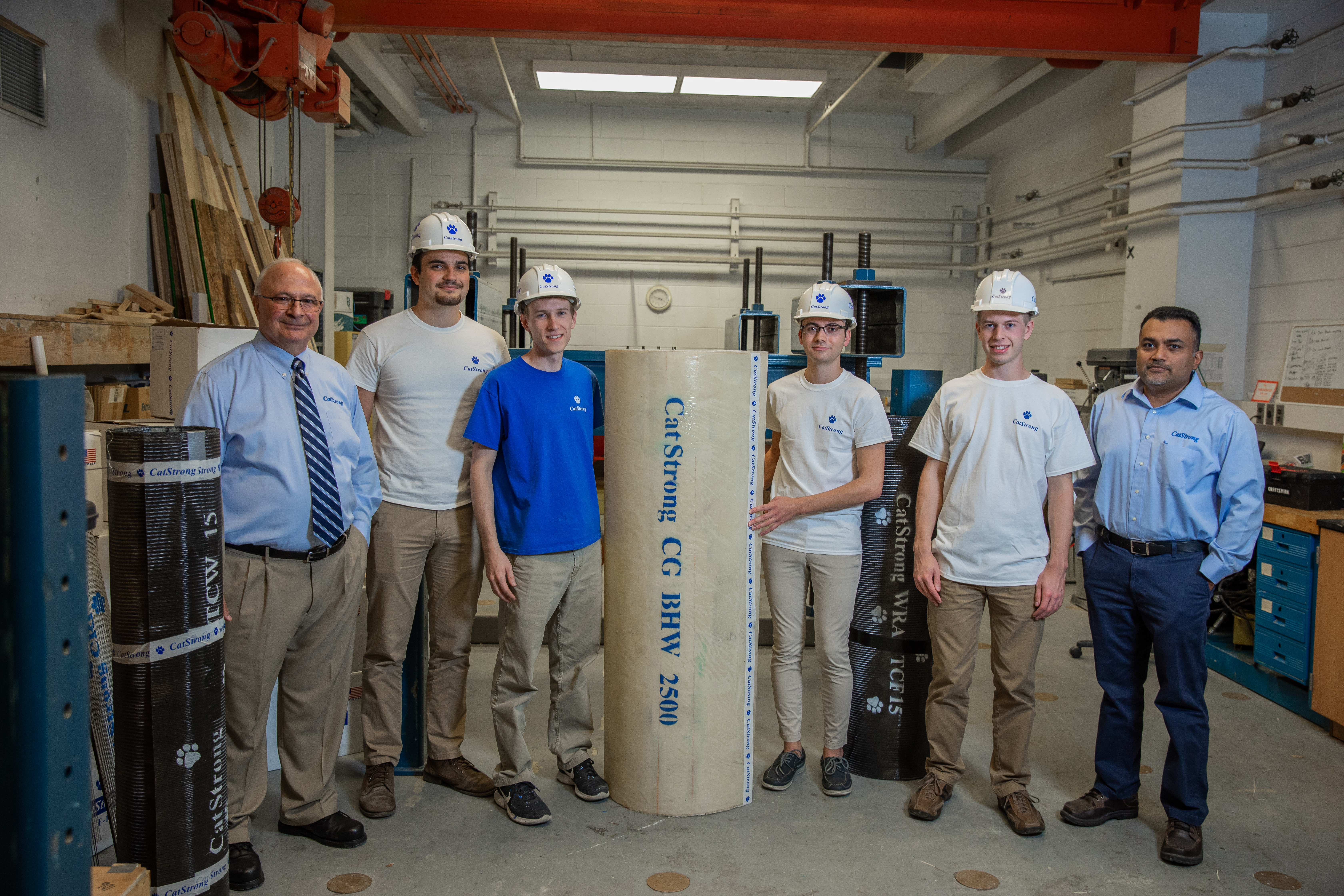 Photo of Dr. Issam Harik and Dr. Abheetha Peiris with four students in the structure’s lab at the University of Kentucky. A reel of Hemp wrap used for pile repair is in the middle of the photo. 